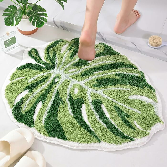 Green leaf-shaped bathroom mat on a white floor with a person stepping on it, enhancing bathroom mats style and comfort.