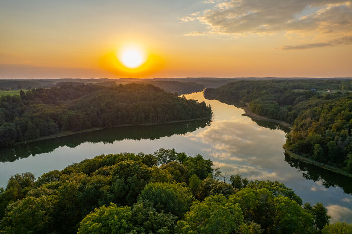 Bird's-eye view of Lithuania showcasing a sunset over a serene river surrounded by lush forests.