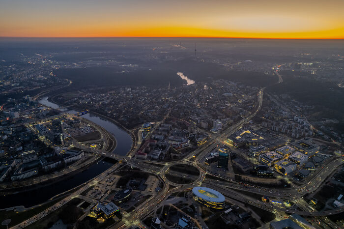 Bird’s-eye view of a Lithuanian cityscape at dusk with winding roads and illuminated buildings.