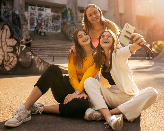 Three friends sitting outdoors taking a selfie, highlighting American social norms that surprise international visitors.