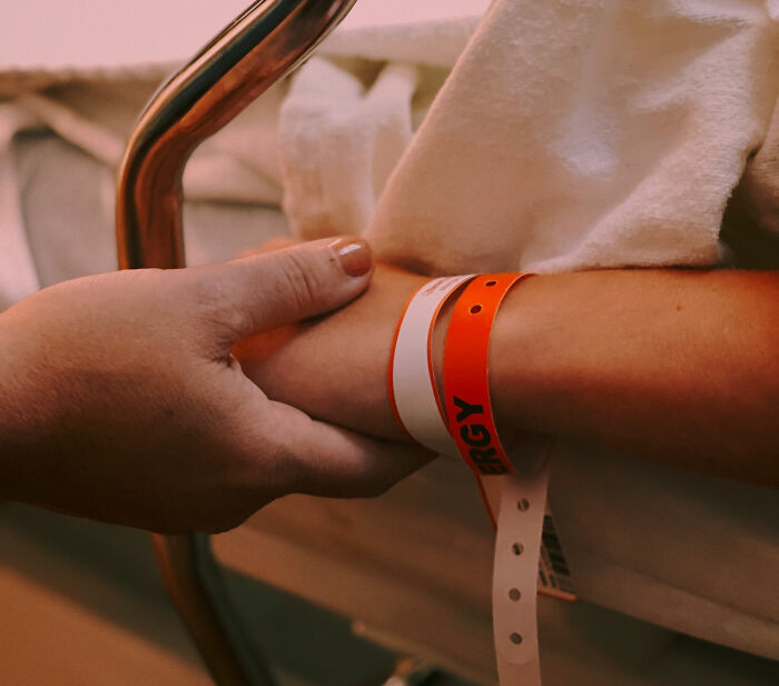 A person with hospital band and hand holding wrist.