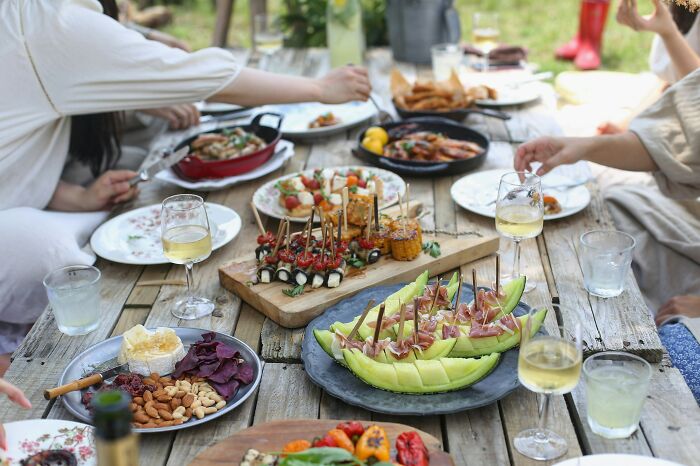 Family event with assorted appetizers on a wooden table, glasses of wine, and people enjoying outdoors.