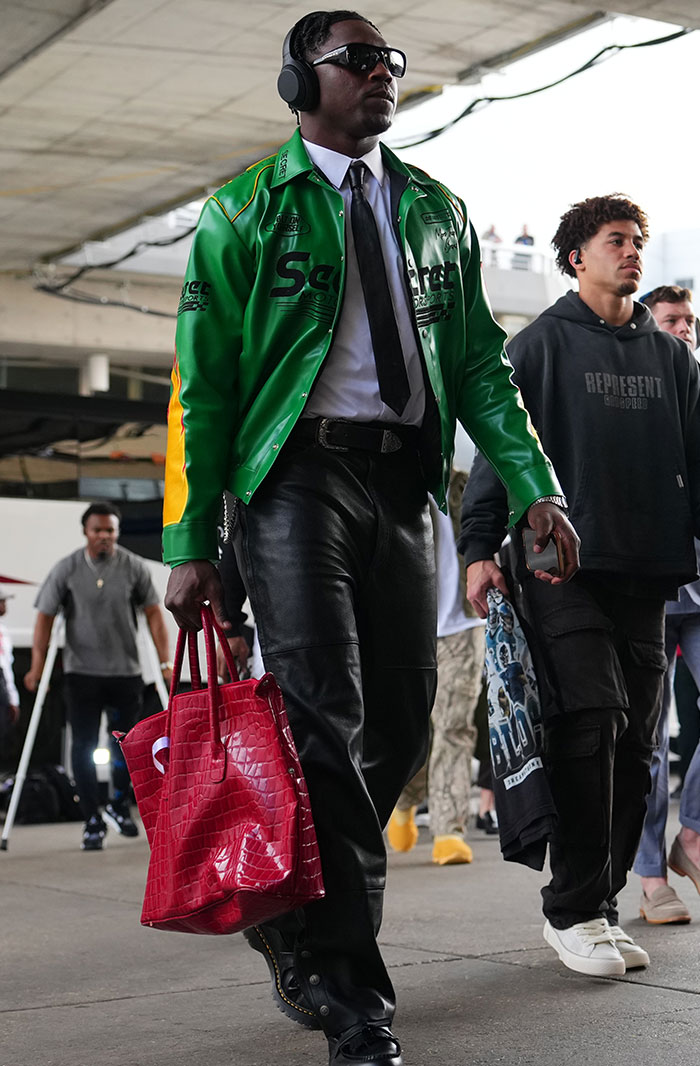 Man in green jacket and leather pants with headphones, carrying a red bag at Super Bowl 2025.