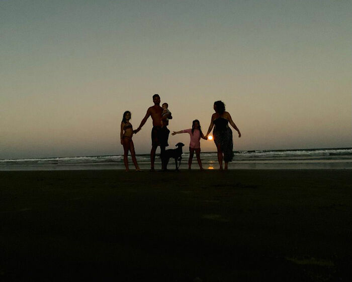 Family with a rescue dog at the beach during sunset, enjoying a peaceful moment together.