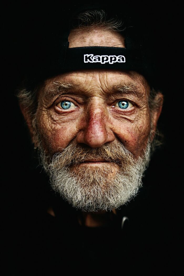 Expressive portrait of an elderly man with striking blue eyes and a beard, wearing a cap labeled "Kappa."