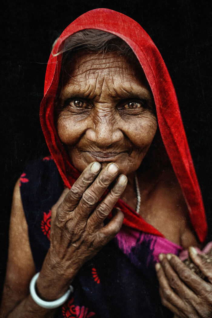 Expressive face captured by photographer, elderly woman with a red scarf, hands near her face, deep wrinkles tell her story.