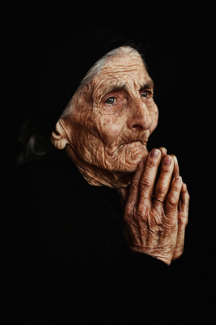 Expressive face of an elderly woman with hands clasped, showcasing deep emotion and storytelling through photography.