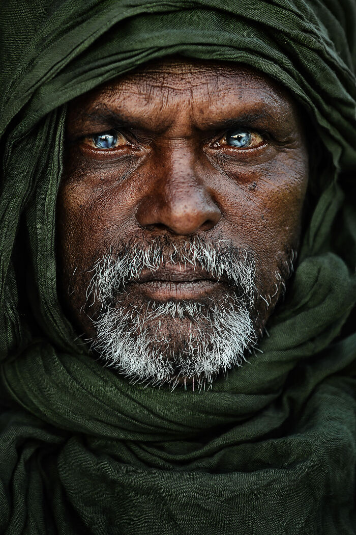 Expressive face of a man in a green robe, with piercing blue eyes and an intense gaze, captured by a talented photographer.