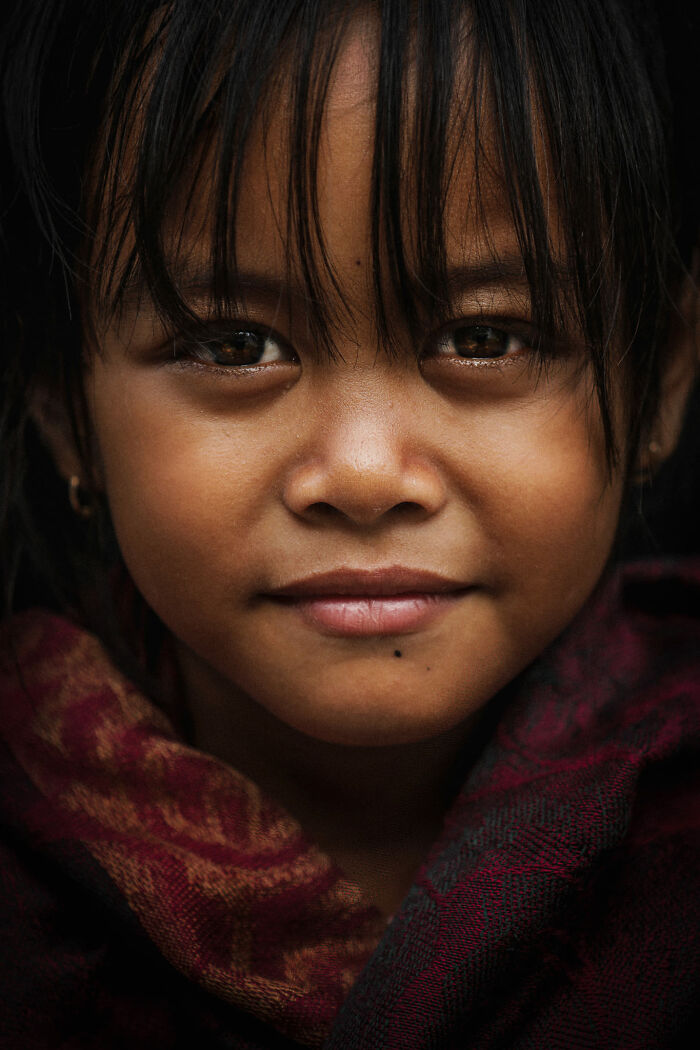 Expressive face of a young girl, gaze intense, wrapped in a patterned shawl.