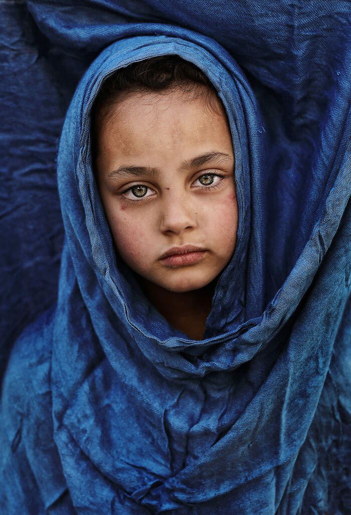 Photographer captures expressive face of a young girl wrapped in a blue shawl, eyes telling their own story.