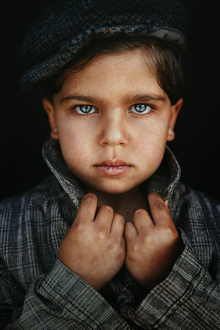 Young child with expressive face, wearing a plaid coat and cap, gazing intently into the camera.