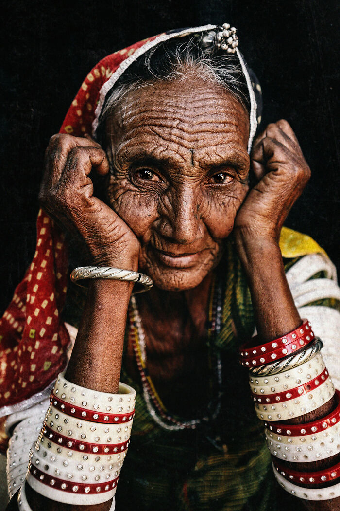 Expressive portrait of an elderly woman with detailed wrinkles, wearing colorful bangles and a headscarf.