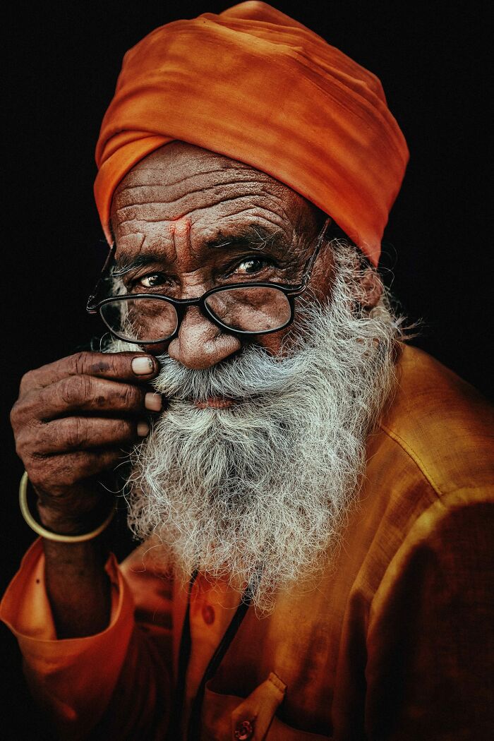 Expressive face captured by photographer, featuring an elderly man with glasses, a white beard, and an orange turban.