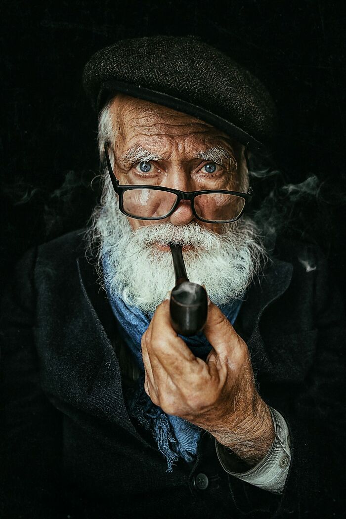 Photographer captures expressive elderly man with glasses and pipe, evoking a sense of wisdom and storytelling.