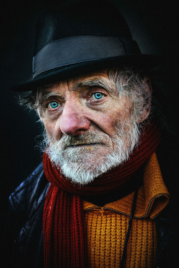 Expressive face of an older man with bright eyes, wearing a hat and scarf, captured by photographer.