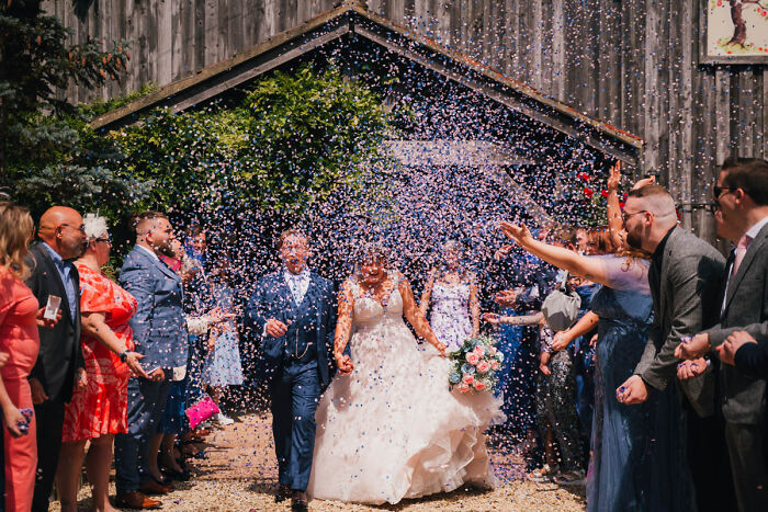 Wedding photographs capturing a couple exiting a rustic barn, showered with confetti, surrounded by guests in vibrant attire.