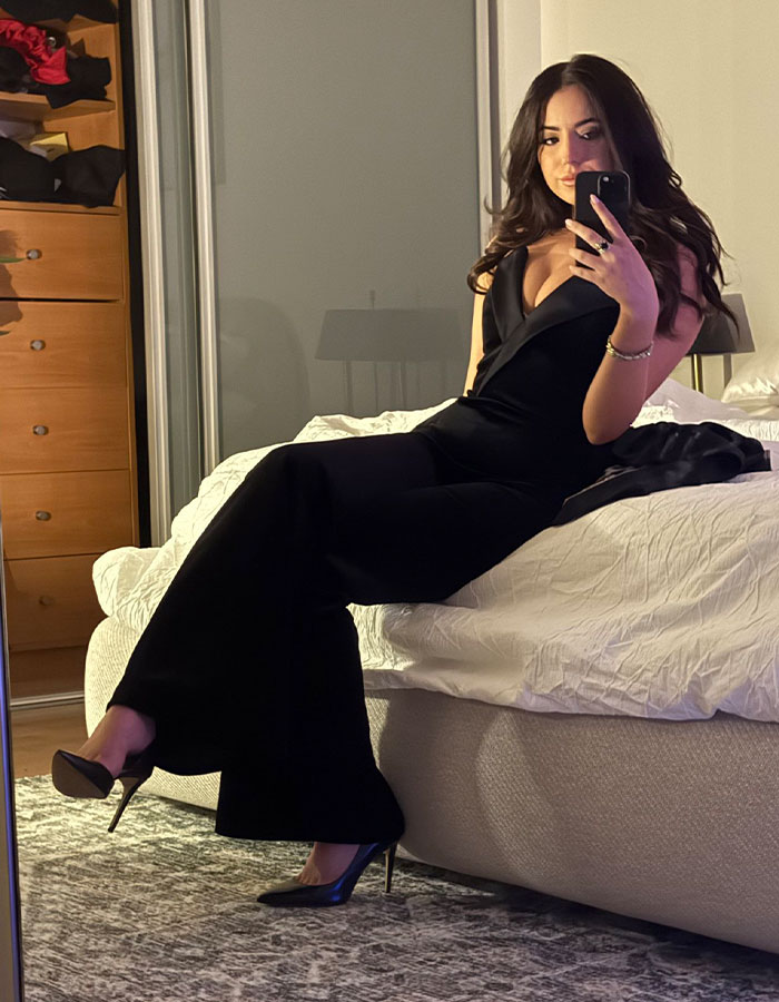 Woman in a black outfit seated on a bed, taking a mirror selfie, related to Elon Musk's 13th child news. Woman in a black outfit seated on a bed, taking a mirror selfie, related to Elon Musk's 13th child news.