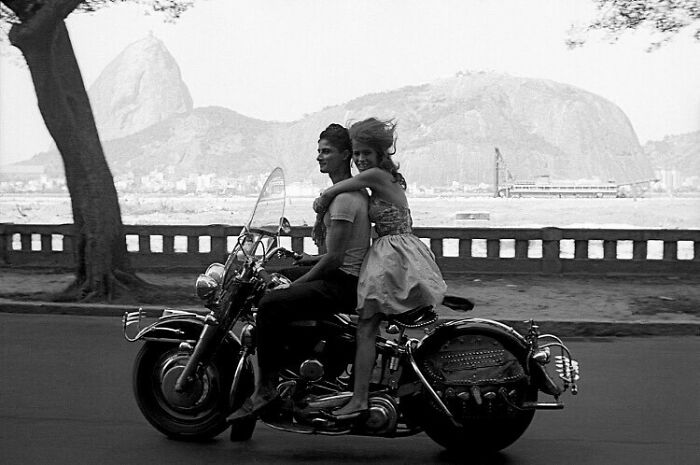 Couple on a motorcycle capturing true happiness, with scenic mountains and a river in the background.