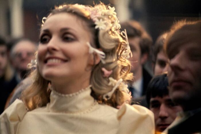 Woman smiling in a crowd, wearing flowers in her hair, capturing a moment of true happiness.