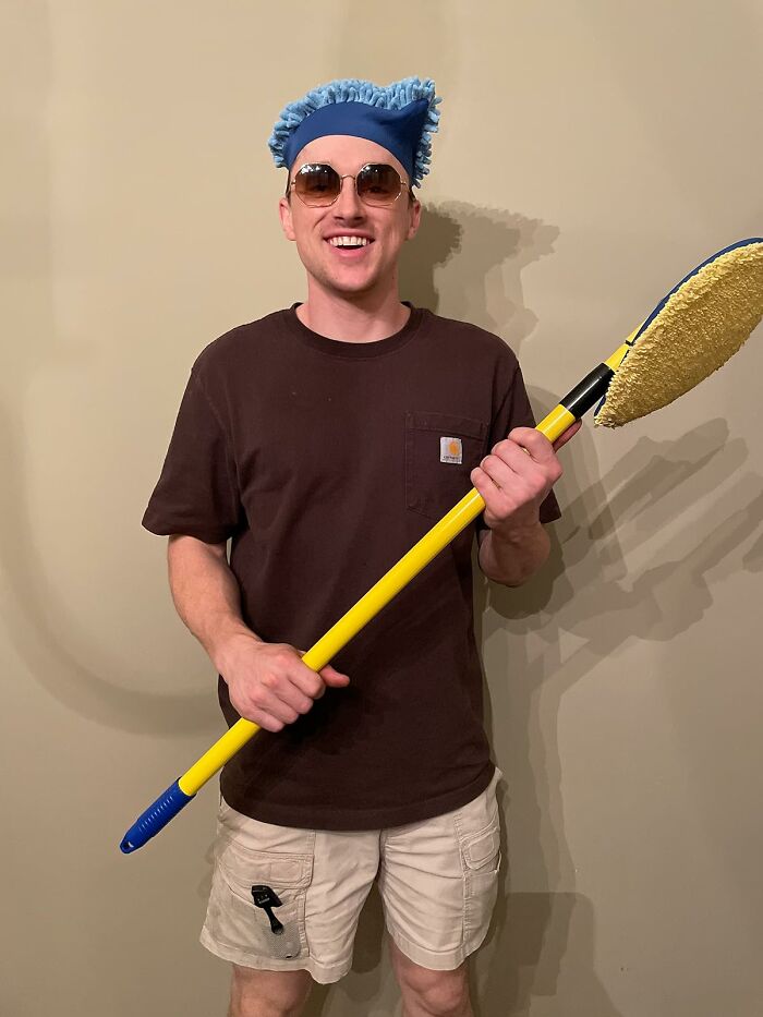 Man smiling in sunglasses and headwear, holding a cleaning mop, ready for a spring cleaning headstart.