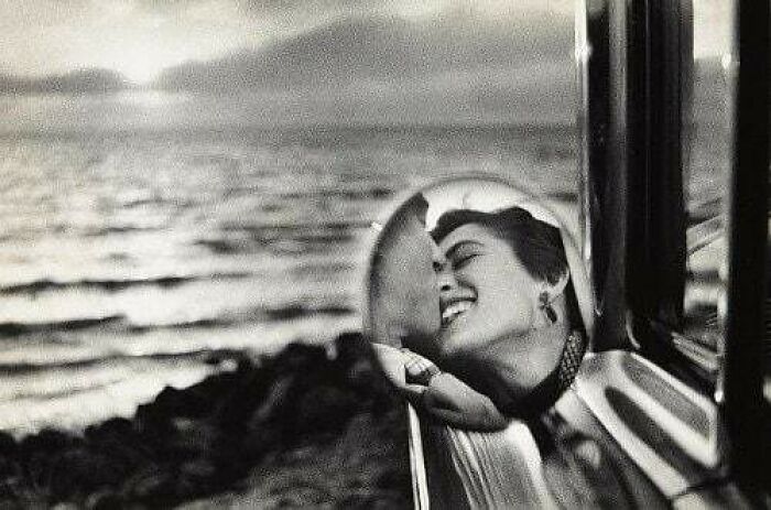 Reflection of a joyful couple smiling by the seaside, capturing true happiness in a car's mirror.