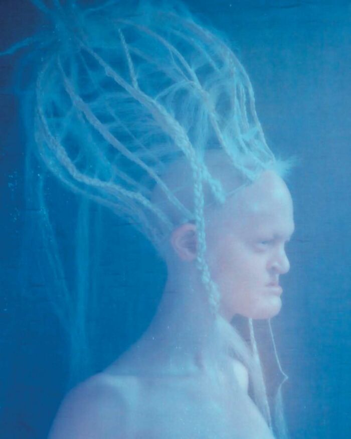 Unique model with intricate hair design against a blue background.