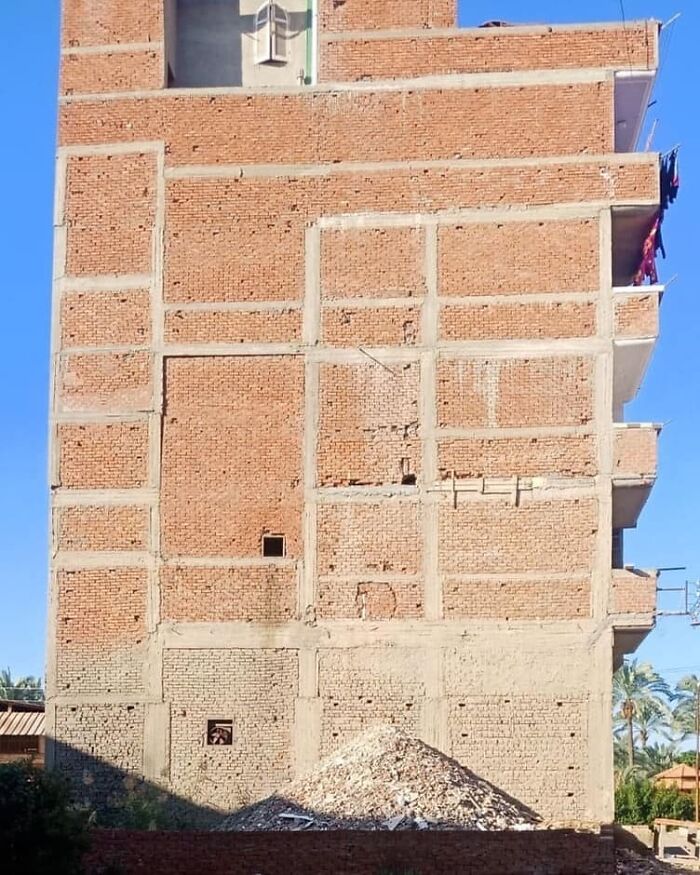 Brick building with misaligned windows and unfinished sections, demonstrating an architecture fail under a clear blue sky.