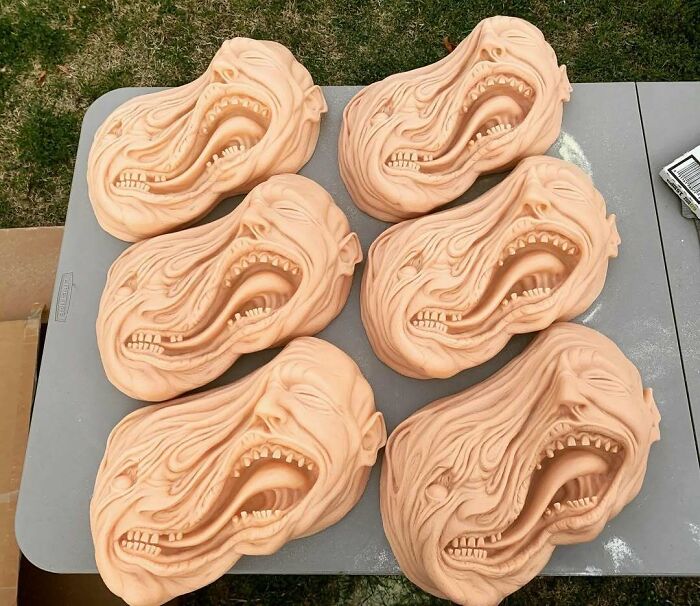Creepy handmade crafts of distorted screaming faces on a table outdoors.