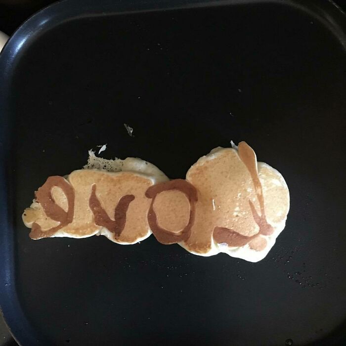 Pancakes on a griddle spelling "love" but misshaped, illustrating humorous Valentines Day fails.