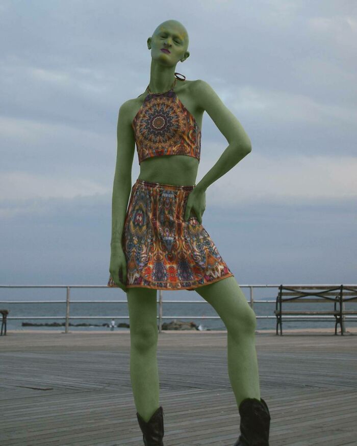 Unique model in a patterned outfit on a boardwalk, posing with an artistic flair against a cloudy sky.