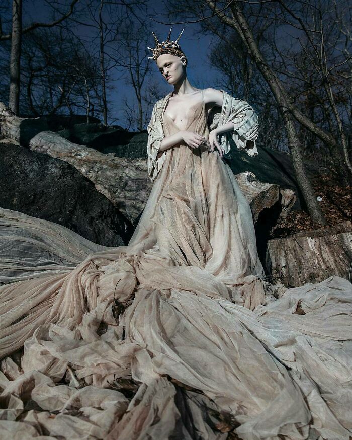 Unique model in an ethereal gown and crown, posing outdoors amidst trees and rocks.