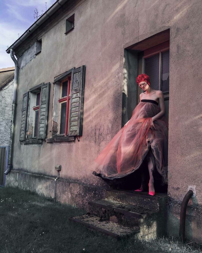 Unique model in a flowing gown standing at a doorway of an aged building, blending elegance with rustic charm.
