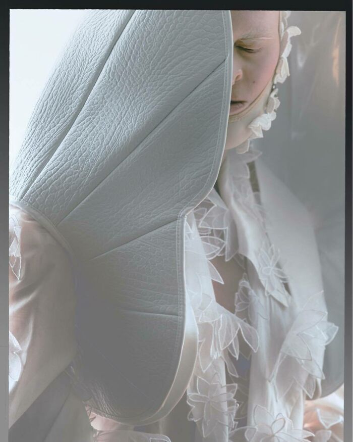 Unique model in elaborate, textured white outfit partially obscures face with avant-garde design.