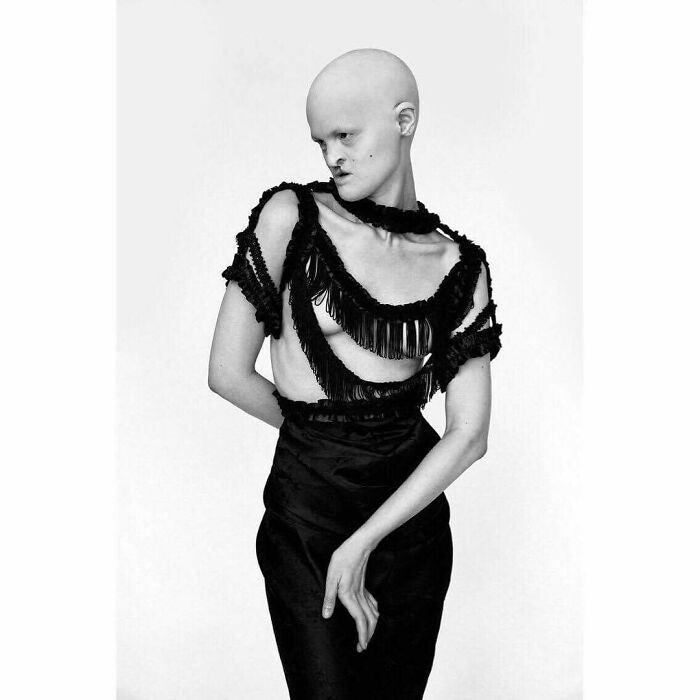 Unique model in a fringed black dress poses confidently against a plain backdrop.