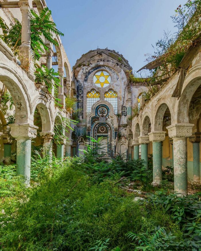 Nature reclaiming an abandoned building with lush greenery overtaking stone arches and walls.