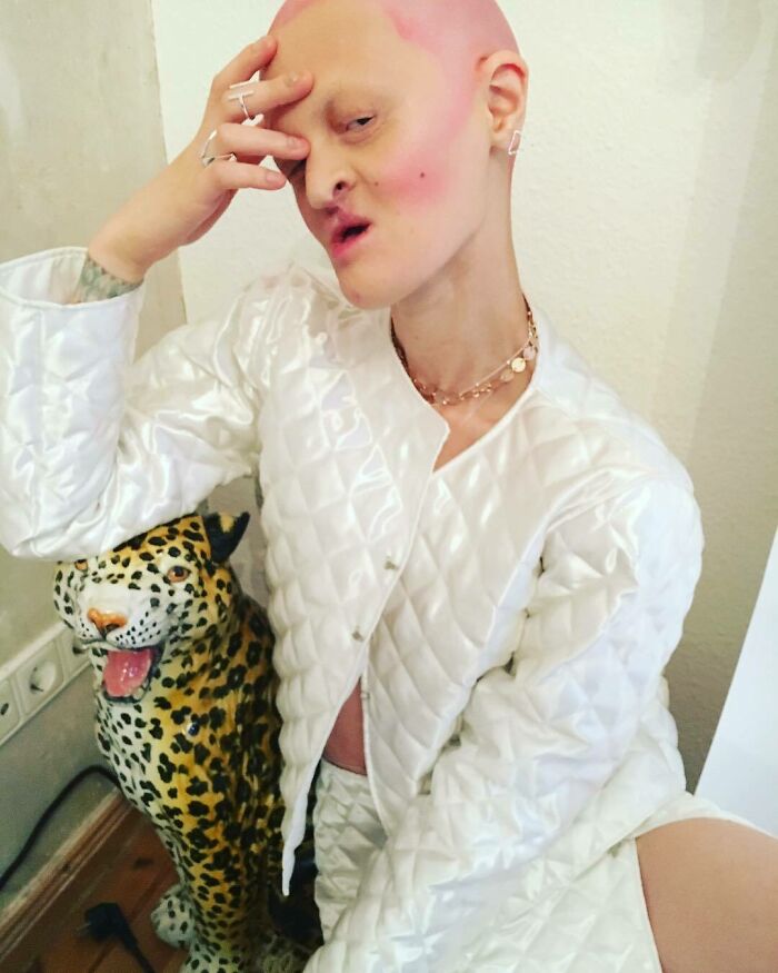 Unique model in quilted outfit posing with a leopard statue, showcasing distinctive style and expression.