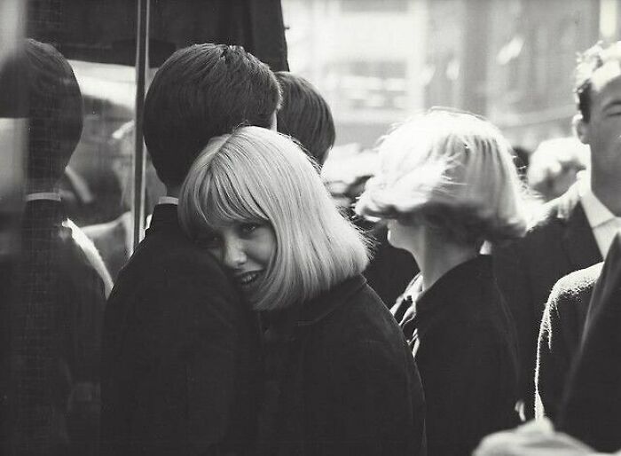 A woman with blonde hair smiles warmly while hugging someone in a crowded street, capturing true happiness.