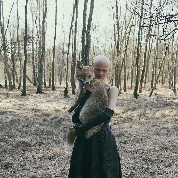 Unique model holding a fox in a forest setting, wearing a black dress.