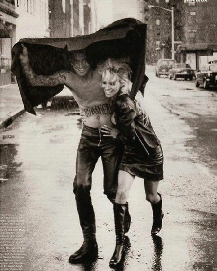 A couple laughing under a jacket in the rain, capturing true happiness on a city street.