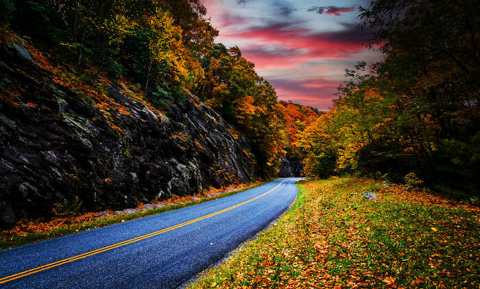 A scenic road with autumn foliage and a vibrant sunset, representing legendary American road routes.
