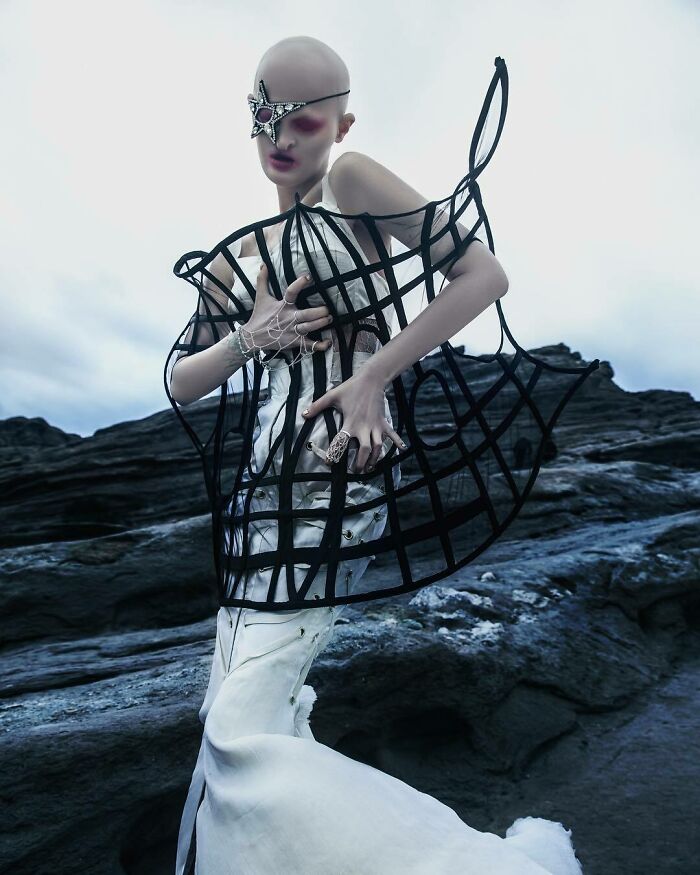 Unique model in an artistic pose wearing avant-garde fashion with a barren landscape backdrop.
