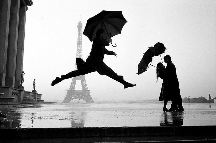 Man joyfully leaping with an umbrella in front of the Eiffel Tower, capturing true happiness.