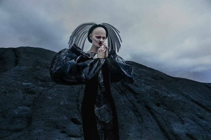 Unique model in avant-garde outfit on a dramatic rocky landscape under a cloudy sky.