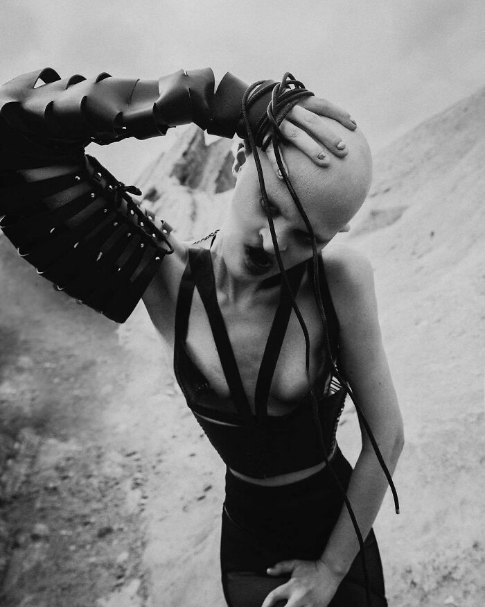 Unique model posing with distinctive fashion elements in a dramatic outdoor setting.