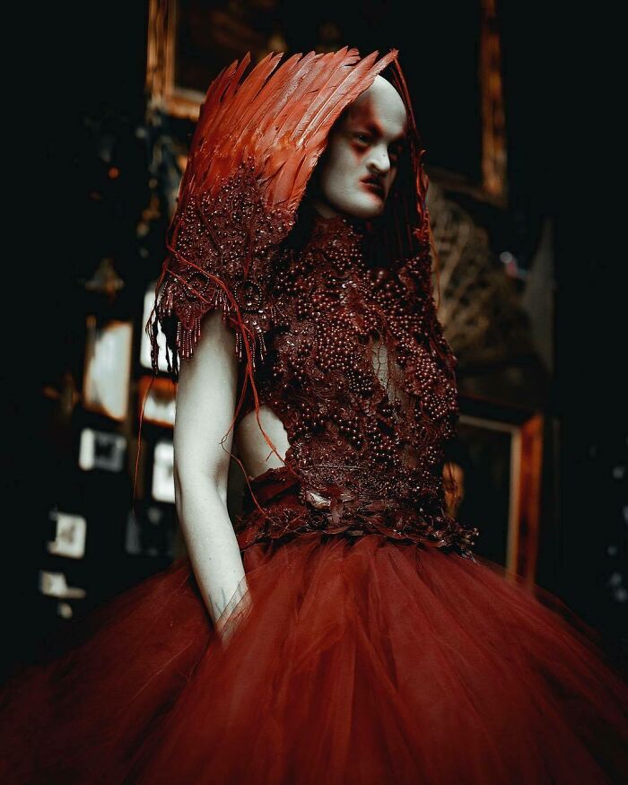 Unique model in a dramatic red gown with feathered details, posed in a moody setting.