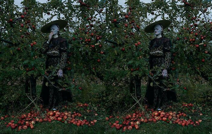 Unique model Melanie Gaydos in ornate attire, standing beside apple trees with scattered fruit.