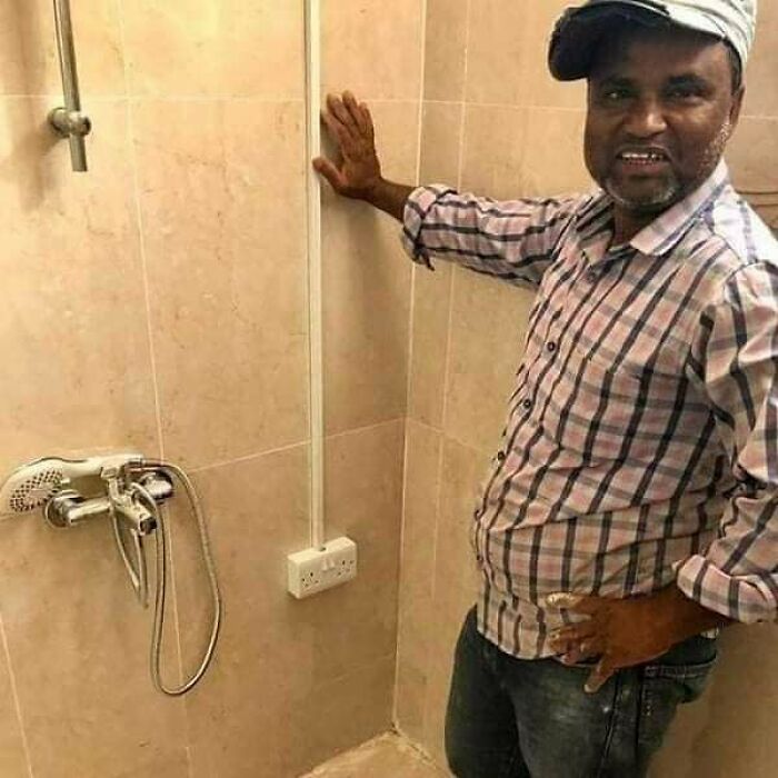 Man showing an architecture fail in a shower with a wall socket dangerously close to the showerhead.