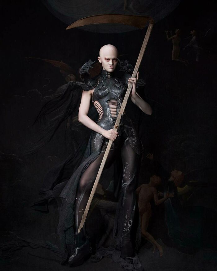 Unique model in an artistic, dark costume holding a scythe in an atmospheric setting.