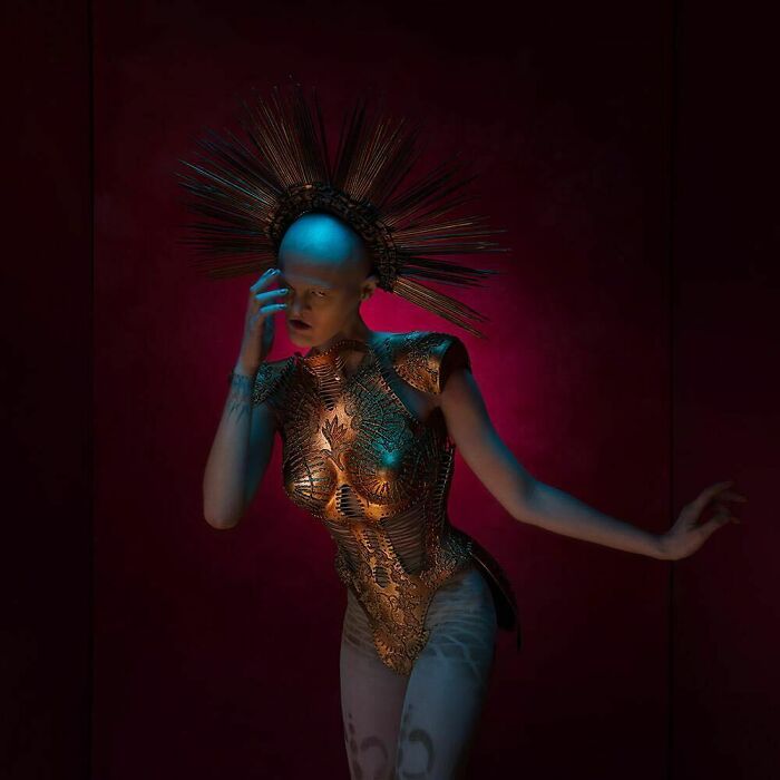 Unique model in ornate costume with spiked headpiece, set against a dark, dramatic background.