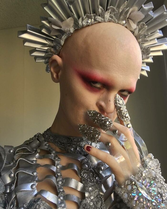 Unique model in metallic attire, with intricate headpiece and dramatic makeup, gazes intensely.